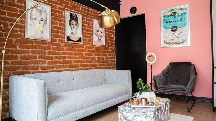 Interior de una casa con sillón y silla, pared de ladrillo rojo y cuadros de actrices famosas