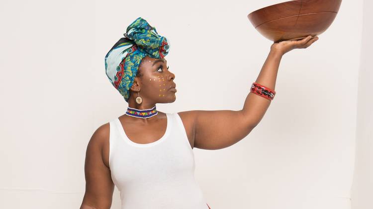 Lion King star Tarisai Vushe, in a headscarf, holds a wooden bowl aloft