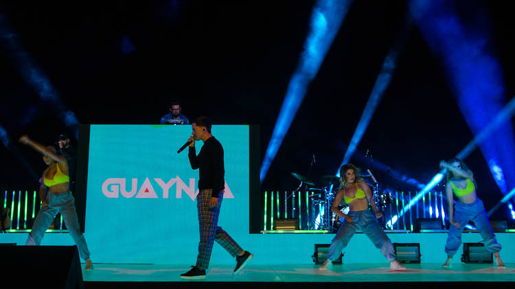 Escenario con luces azules y el cantante Guaynaa con microfono