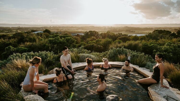People bathing in a rocky hot spring in scrub land