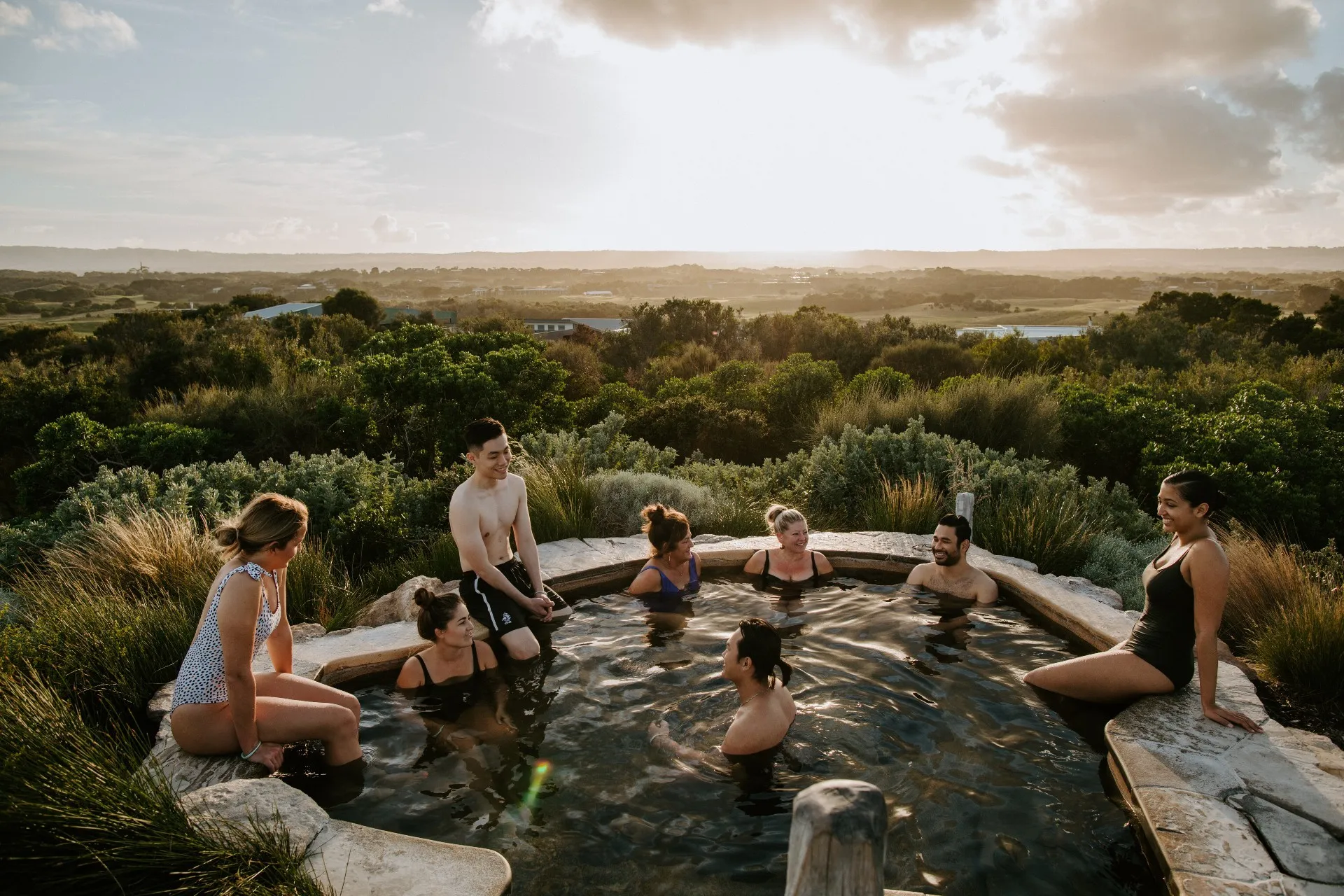 People bathing in a rocky hot spring in scrub land