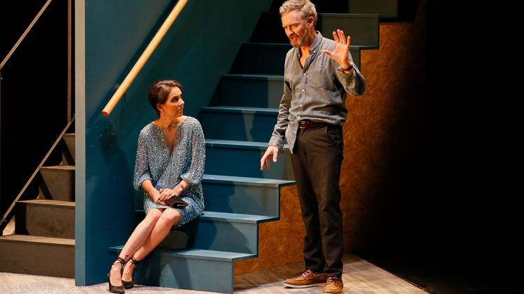 A woman sits on a staircase while a man talks to her