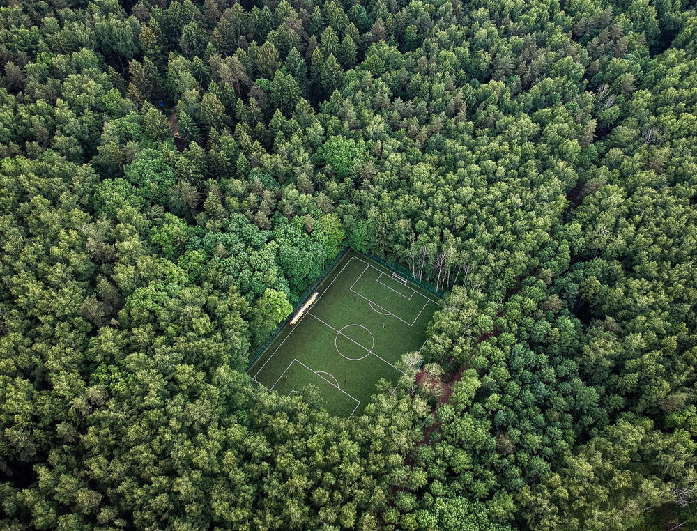 Aerial shot of a green football pitch completely surrounded by dense, tall green trees