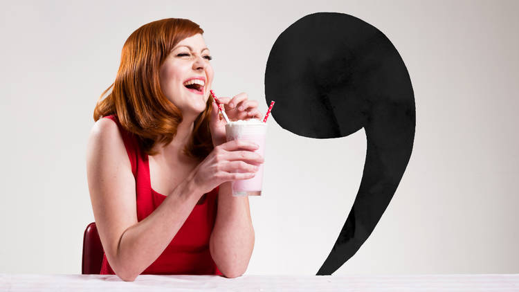 A woman with red hair and wearing a red dress laughs while drinking a milkshake with two straws. Next to her is a person-sized comma posed to look like it is drinking from the other straw like they're on a date.