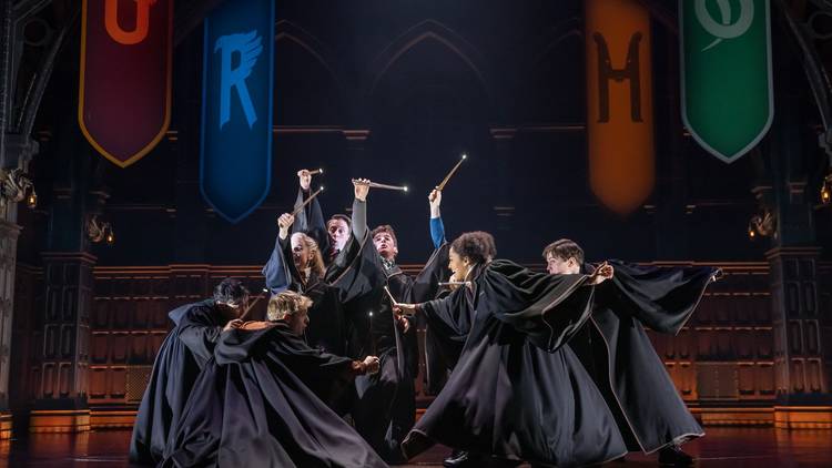 Cast members in black robes dancing around with wands.