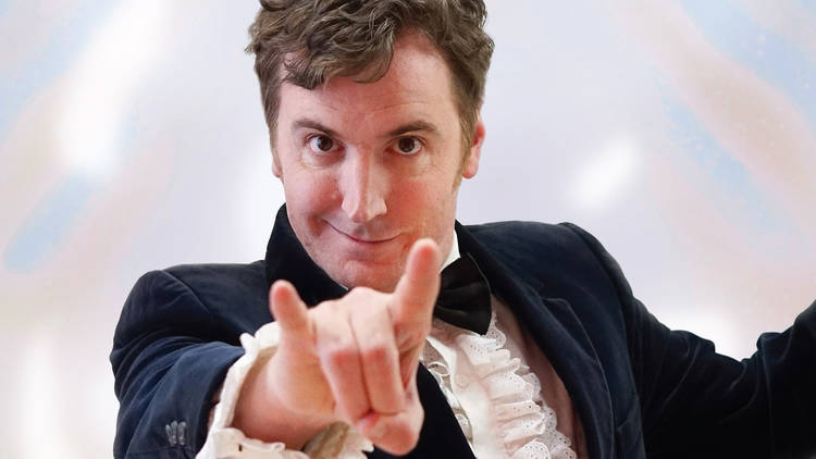 A close up shot of a man wearing a dinner suit with a bowtie and white ruffled shirt underneath it