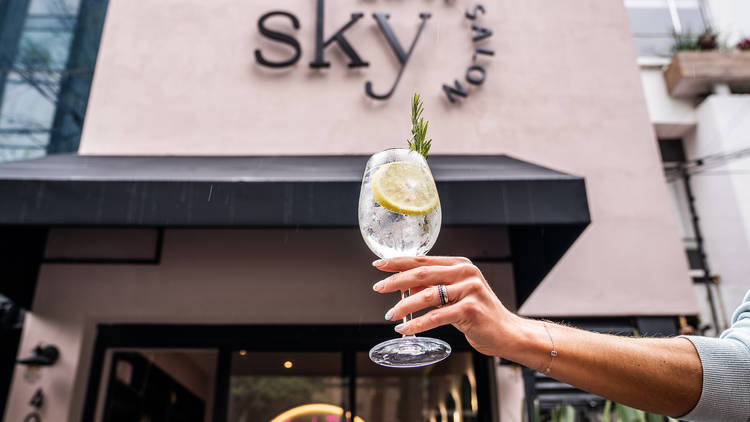 Copa de gin tonic y de fondo local de Sky Nails Salon