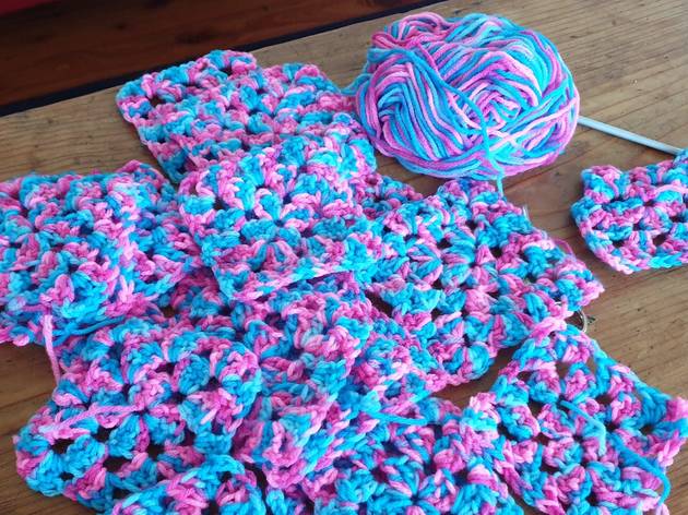 Crochet A ball of wool sits next to a pile of crochet granny squares and a crochet hook.