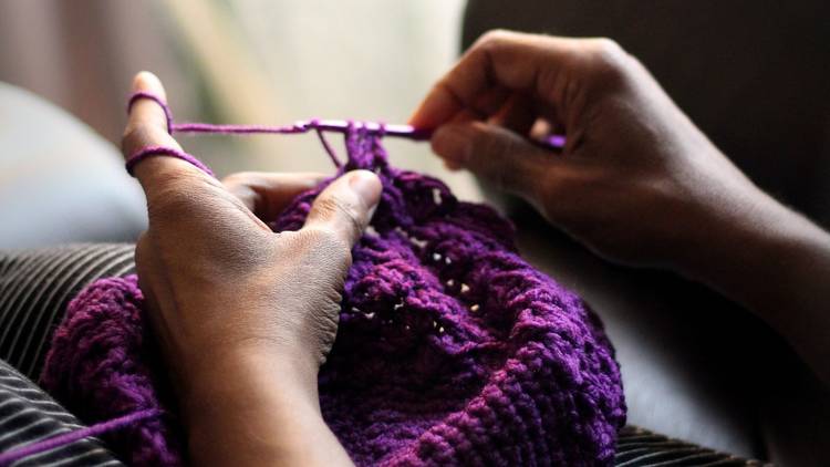 Close up on a person's hands as they crochet something from purple wool.