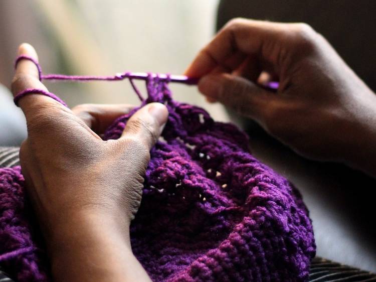 Close up on a person's hands as they crochet something from purple wool.