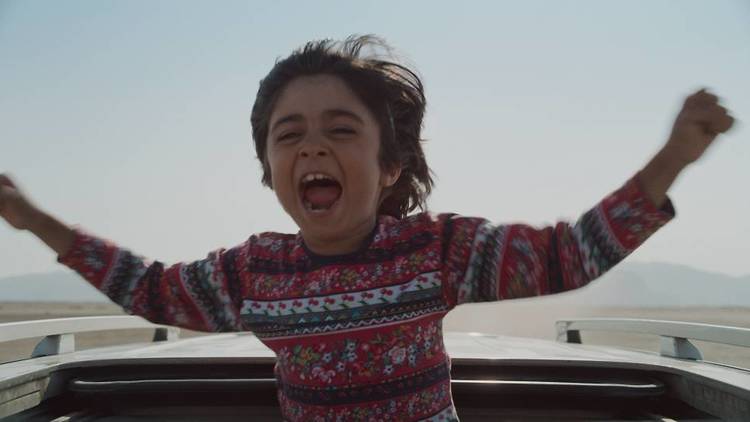 an excited young boy in a chunky knit sweater hands out the sun roof of a car
