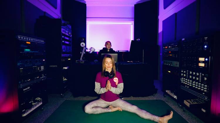 Angel sits on yoga mat with hands in prayer position, she is in a music studio