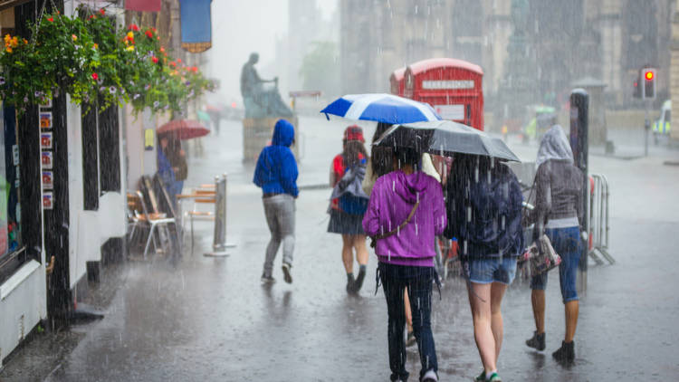 Group of girls hurry at the rain with umbrella in the city