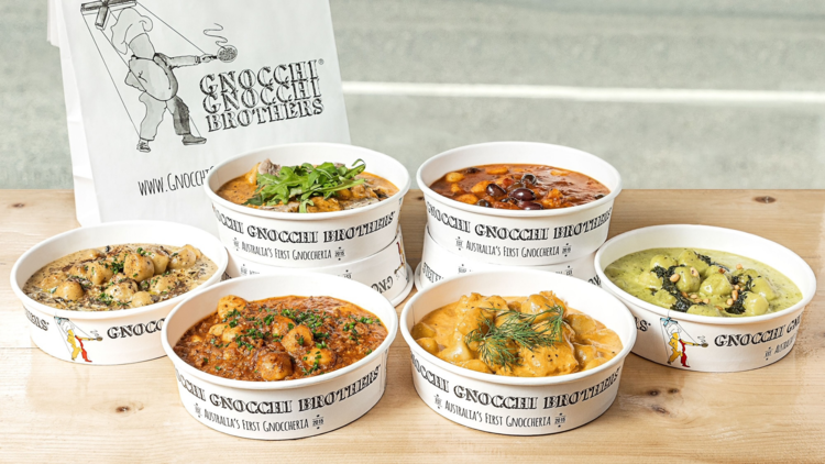 A series of round take away tubs holding various gnocchi recipes on a wooden table