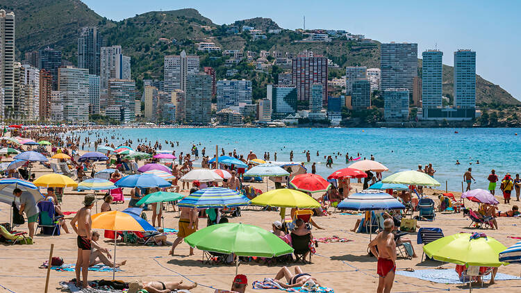 Crowds of people undernearth multicoloured beach umbrellas on a sandy beach in Benidorm