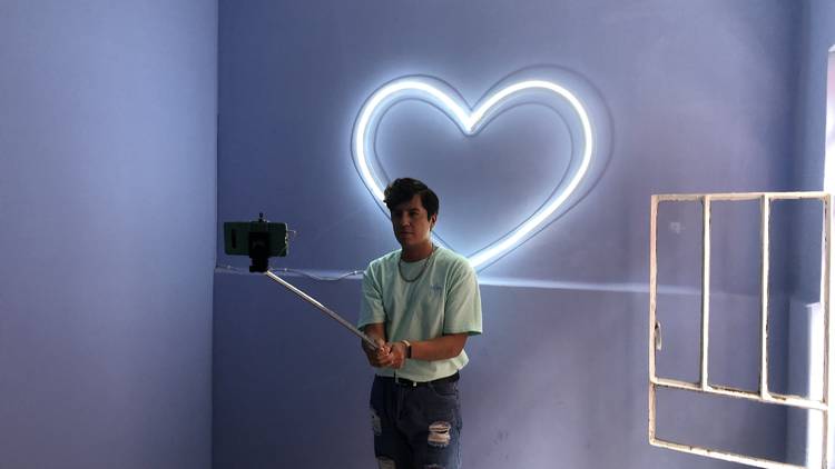 Persona tomándose una selfie en una pared azul con luz neón en forma de corazón
