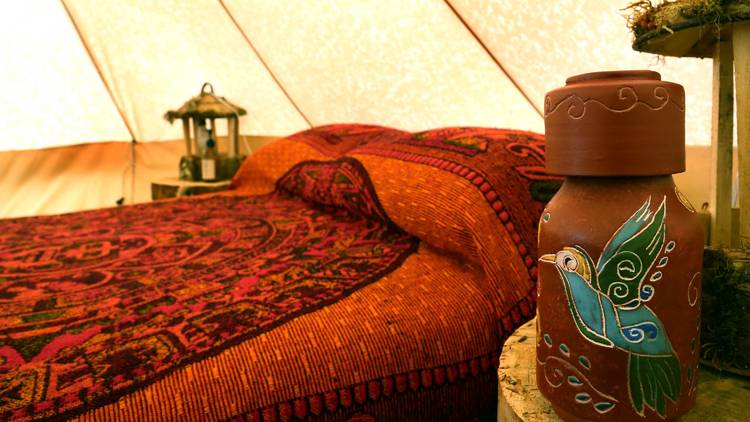 Interior de glamping con cama de cobija roja y artesanías mexicanas alrededor