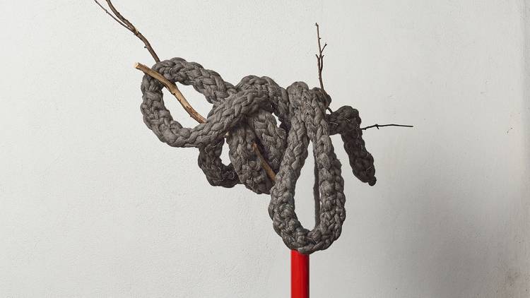 A braided grey rope made of steel wool and mesh is draped over a tree branch coming out of a red pole