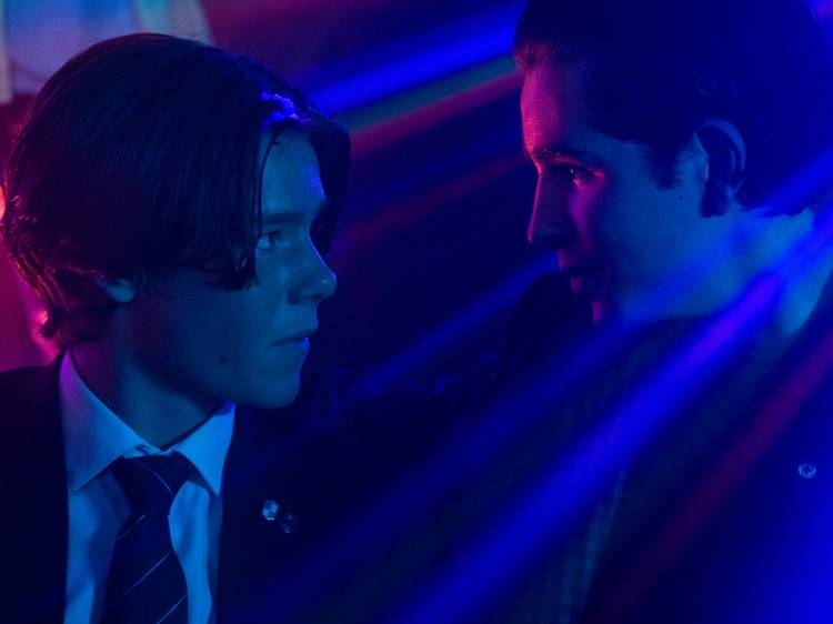 The two leads of Young Royals gaze at each other in a club with blue light