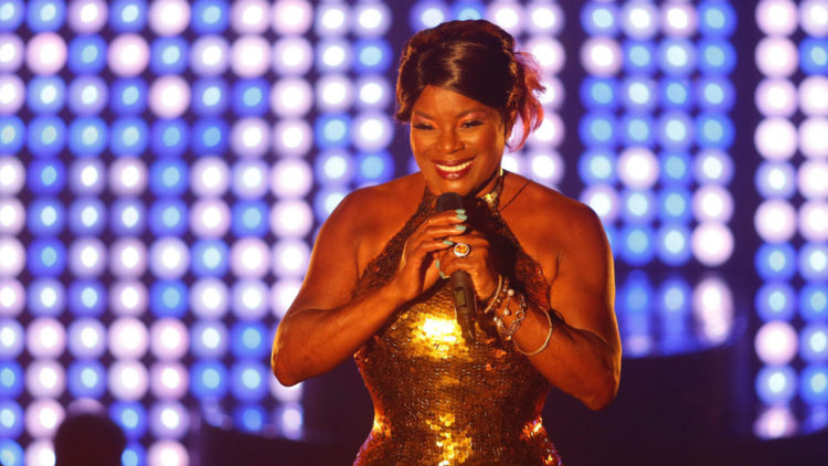 Marcia Hines in a gold dress holding a microphone