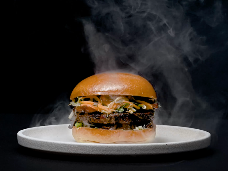 A brioche bun with pickled carrots and mushroom patty on a white plate surrounded by smoke whisps