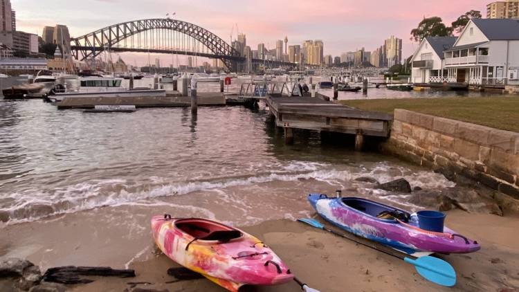 Two kayaks lie in the sand in front of the Sydney Harbour Bridge