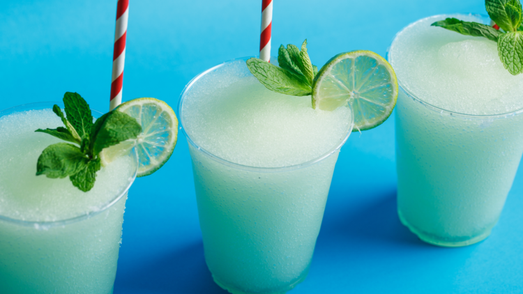 Three frozen margaritas with red and white straws on a blue background