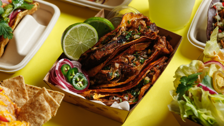 Carnitas tacos in a box on a yellow background