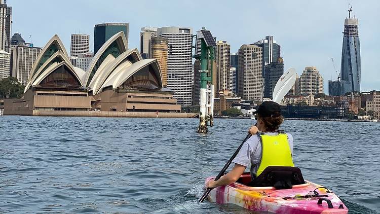 A kayak paddling in front of the Sydney Opera House