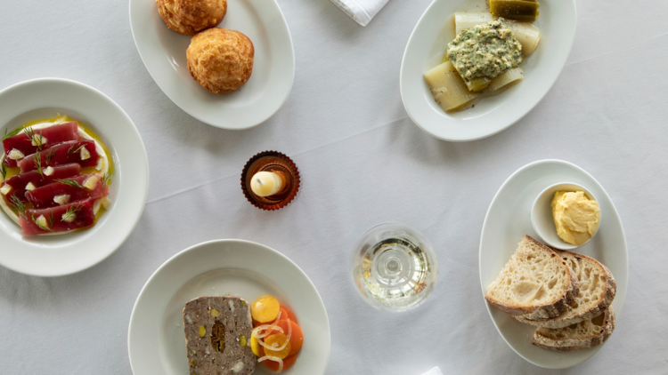 A white table with 5 plates, sliced tuna, terrine, pasta and bread