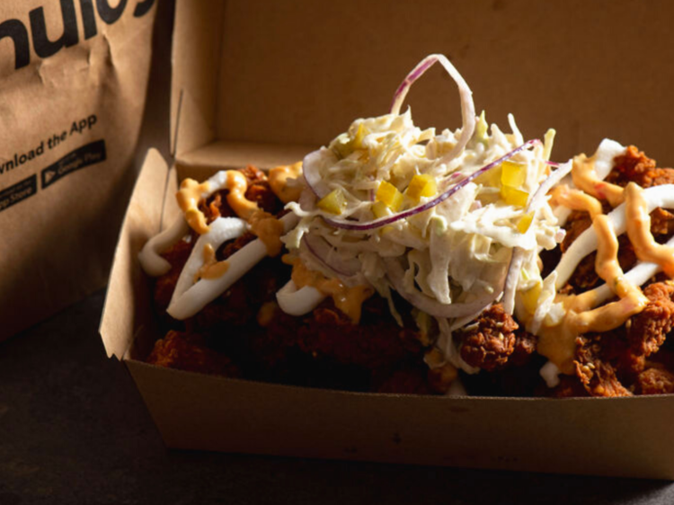 A cardboard take away box with fried chicken, creamy light slaw and diced pickles. Menulog paper bag in background.