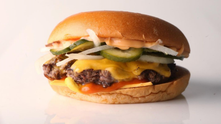 A burger with pickles, onion, cheese, tomato sauce on a white reflective background