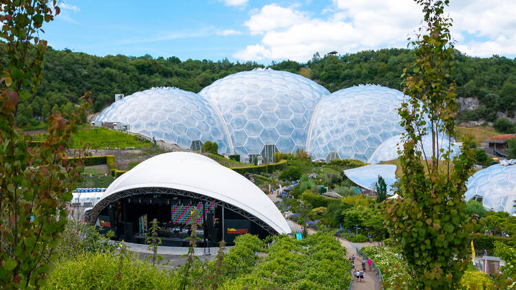An outdoor stage set up for a concert in front of the geodesic biodomes at the Eden Project, on a sunny day