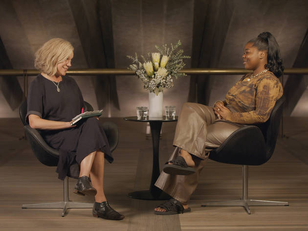 Edwina Throsby interviews FlexMami for Ideas at the House Edwina Throsby sits across from FlexMami, there is a table with a vase of flowers between them, they smile at one another.