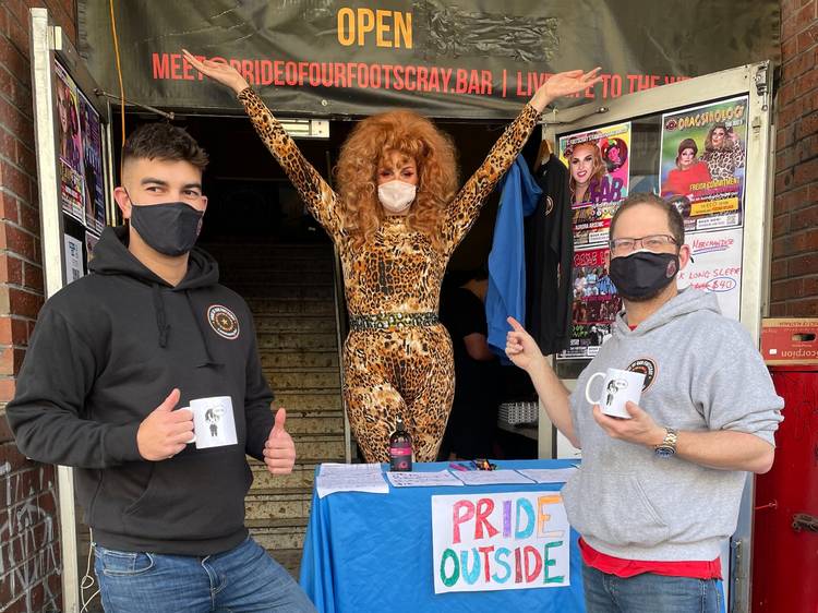 Two people wearing masks smile after getting drinks from a drag queen