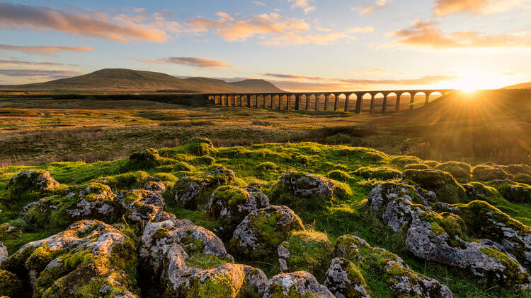 Gorgeous golden light as the sun sets behind the Ribblehead Viaduct with rocks in foreground.