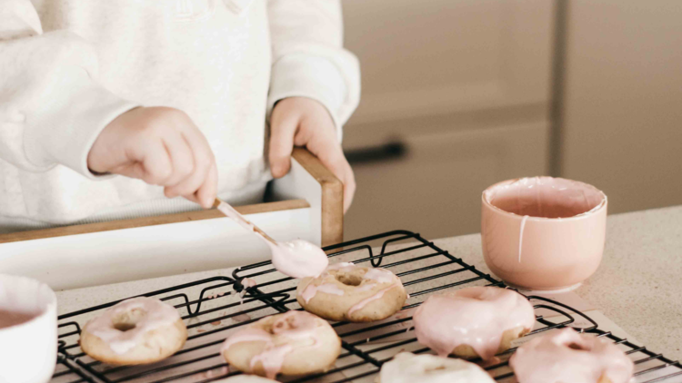 A child putting frosting on donuts. 