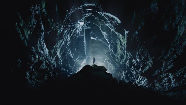 A stunning shot of a man in the distance in an underground cave that's lit up eerily blue