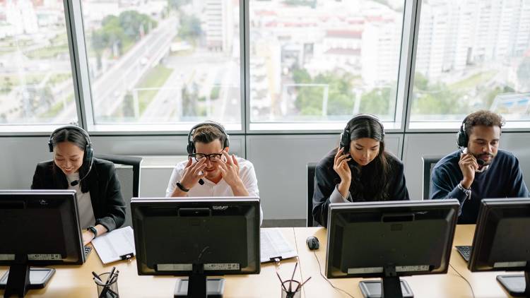 Four people sitting at computers and wearing headsets.