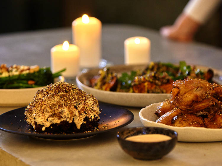 a stone bench with 4 plates of food, roasted cauliflower, chicken, glazed pumpkin and broccolini 