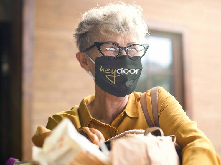 An elderly woman wearing a mask that says 'Heydoor' while carrying groceries.