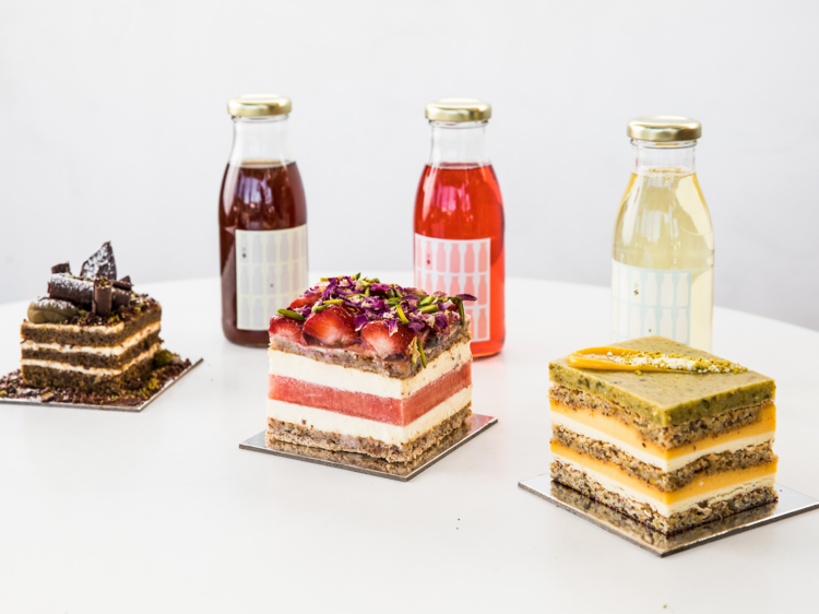 Three cakes sit in front of three bottled cocktails on a white table