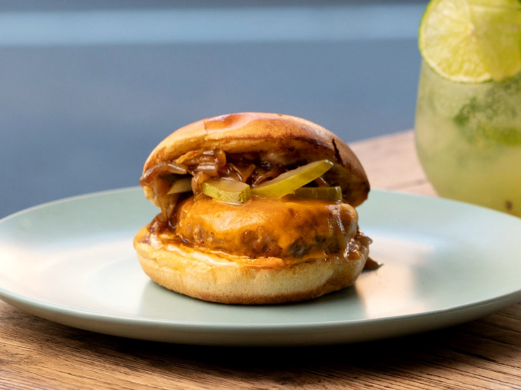 a white plate with a cheeseburger on it, a mojito in the background