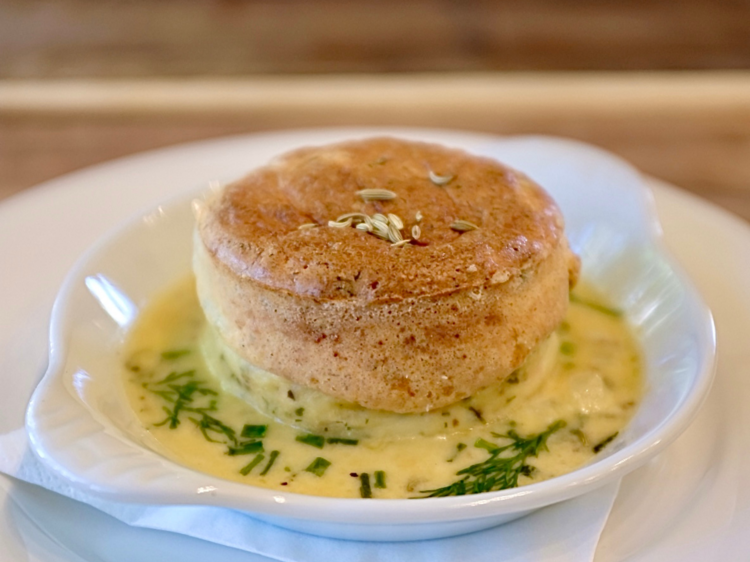 A crab souffle on a white plate with a butter sauce and herbs