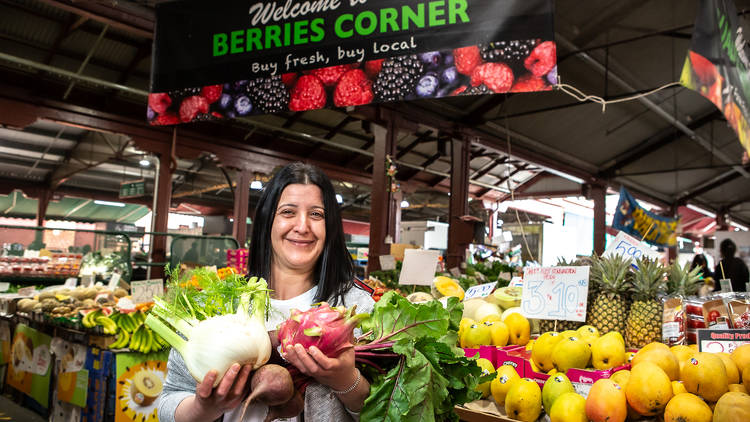 A woman holding veg and fruit in front of Queen Victoria Market.