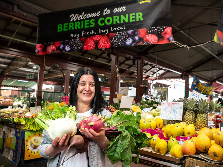 A woman holding veg and fruit in front of Queen Victoria Market.