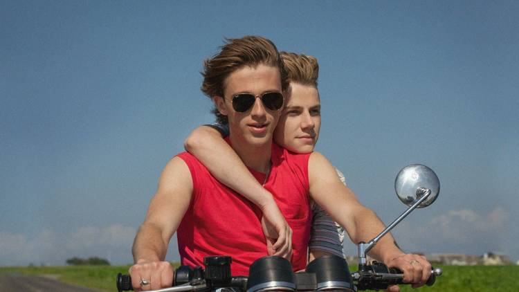 Two boys on the back of a motorbike against blue skies