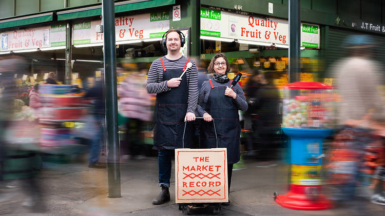Two people holding microphones stand in front of a green grocer