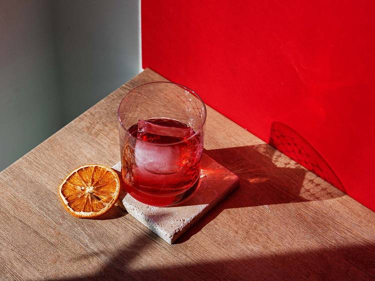 On a pink background, negroni cocktail in a glass from a black drink sack