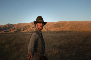 Benedict Cumberbatch in a cowboy hat in a Wild West setting with scrub and sandy hills